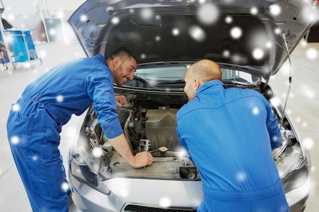 Foto serviço de reparação de automóveis manutenção e conceito de pessoas mecânico homens com chave inglesa reparando carro na oficina sobre a neve