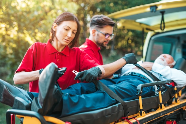 Foto serviço médico de emergência no trabalho. o paramédico está puxando a maca com um homem sênior com ataque cardíaco grave para o carro da ambulância. ajuda na estrada. conceito de assistência de motoristas.