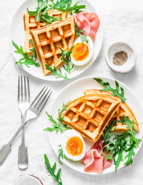 Servido café da manhã com batatas waffles salgados presunto de ovo cozido e rúcula na luz de fundo