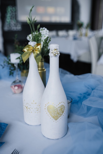 Serviert für Hochzeitsbankett Tisch in blau weiß. Hochzeitsdekoration. Blaue Serviette mit Blume auf einem weißen Teller. Goldene Flaschen sind Vasen für Blumen. Dekorierte Flaschen Champagner.