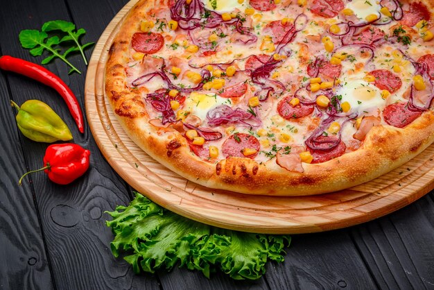 Serviert köstliche Pizza mit Wachteleiern, Schinkenwurst und Gemüse auf schwarzem Hintergrund