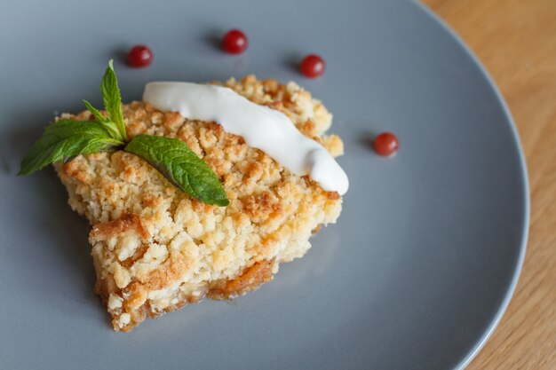 Serviert Scheibe frisch gebackenen hausgemachten Apfelkuchen mit Sahne und Beeren auf einem grauen Teller