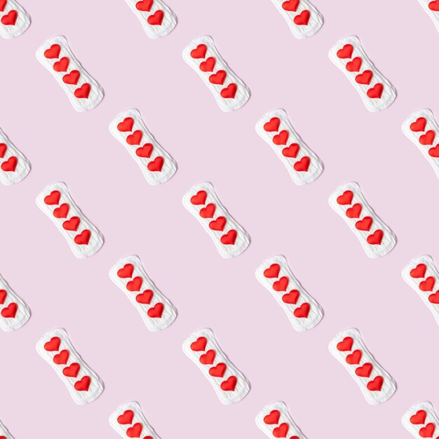Foto servilleta sanitaria de algodón blanco de patrones sin fisuras y corazones rojos en forma de gotas menstruales sobre un fondo rosa pastel vista superior plana minimalismo ciclo menstrual concepto de salud de la mujer