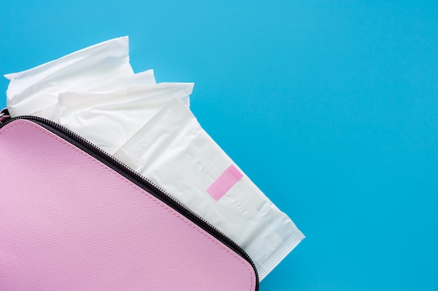 Servilleta sanitaria en bolso rosa de mujer sobre fondo azul