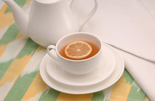 En una servilleta taza de té con limón en un platillo y tetera