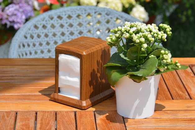 Un servilletero de madera con una flor blanca se sienta en una mesa afuera.