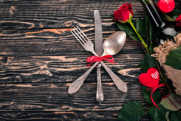 Servindo a mesa para comemorar o dia dos namorados. Talheres, prato, rosas. Em um fundo de madeira. Vista do topo. Espaço livre para o seu texto.