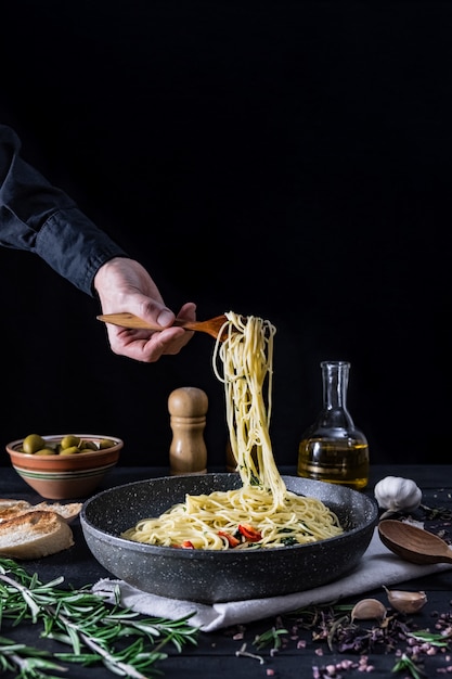 Servindo massas italianas da panela, copie o espaço. Refeição tradicional de espaguete com legumes e azeitonas na superfície rústica preta