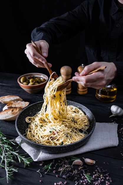 Servindo massas italianas tradicionais de uma panela. Masculinas mãos tomando espaguete na colher e um garfo, filmado em baixa chave