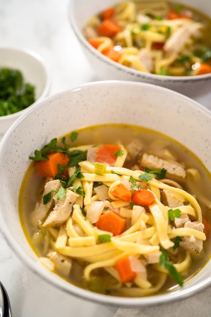 Servindo sopa de macarrão de galinha com macarrão kluski em tigelas de sopa de cerâmica branca