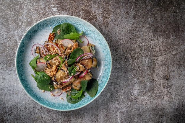 Servindo um prato do menu de um restaurante. Berinjelas recheadas com cebola, espinafre verde e nozes em um prato no fundo de uma mesa de pedra cinza