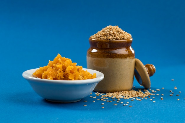 Sesam im Tontopf mit Jaggery in der Schüssel auf blauem Hintergrund