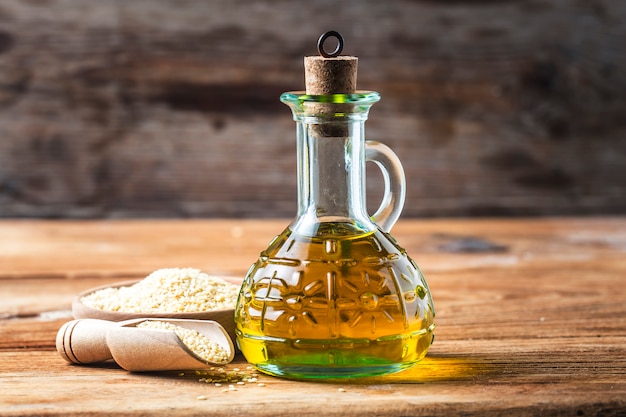 Sesamöl und Flasche mit Öl auf einem alten Holztisch? Sesamöl in einem Glaskrug.