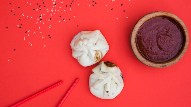 Foto sesamsamen; essstäbchen; knödel und saucen in holzschale auf rotem hintergrund