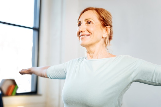 Sesión de entrenamiento por la mañana. Feliz y guapa dama en forma con amplia sonrisa extendiendo sus manos durante el entrenamiento matutino