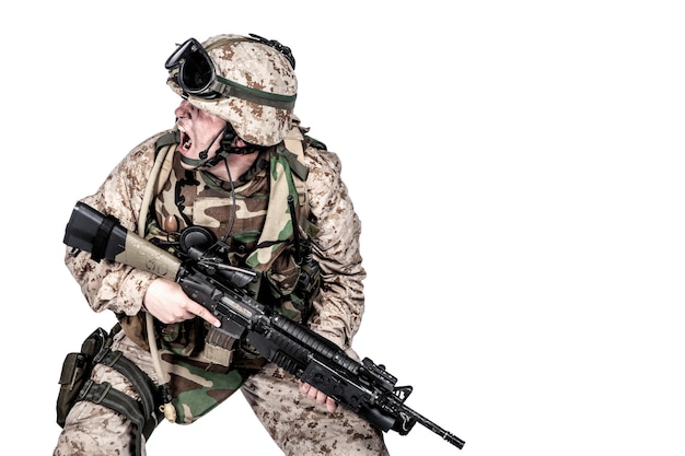 Sesión de estudio de soldado de infantería moderno, fusilero de la marina estadounidense en uniforme de combate, casco y armadura corporal, gritando y agachándose con rifle de servicio de asalto en manos aisladas sobre fondo blanco