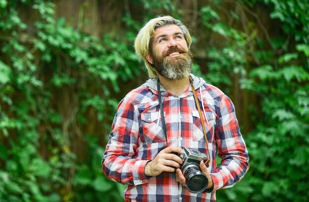 Sesión de fotos al aire libre brutal hombre viajero con fotografía de cámara retro en la vida moderna consejos de viaje fotógrafo profesional uso cámara vintage hombre barbudo hipster tomar foto vacaciones idílicas