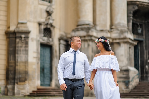 Sesión de fotos de boda en el fondo de la antigua iglesia. La novia y el novio están caminando juntos. Un hombre toma la mano de una mujer. Fotografía de boda de estilo rústico o boho