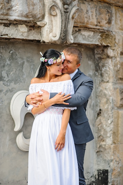 Sesión de fotos de boda en el fondo del antiguo edificio. La novia y el novio se abrazan suavemente.