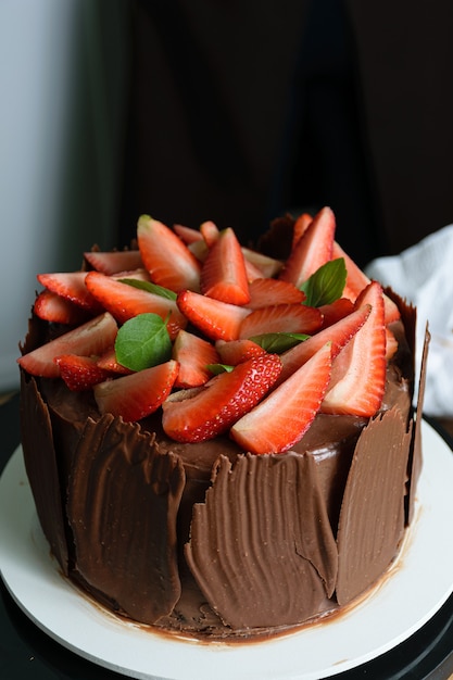 Sesión de fotos con tarta de chocolate decorada. Pastel de chocolate cubierto con fresas, hojas de albahaca fresca, mermelada de moras y platos de chocolate alrededor.