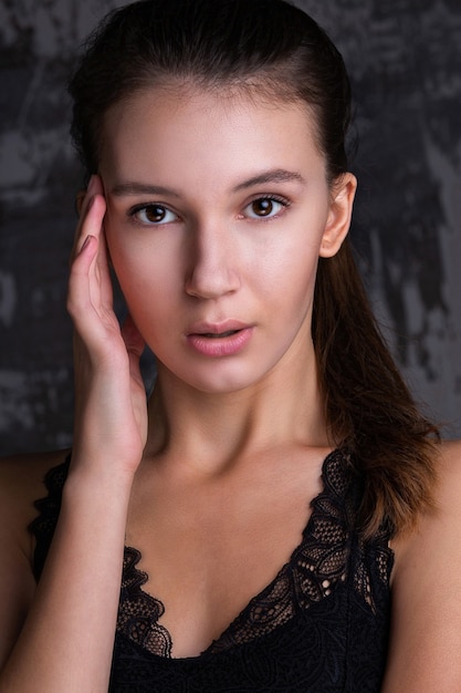 Foto sesión de prueba de la hermosa modelo morena con una piel perfecta y maquillaje natural posando contra la pared gris