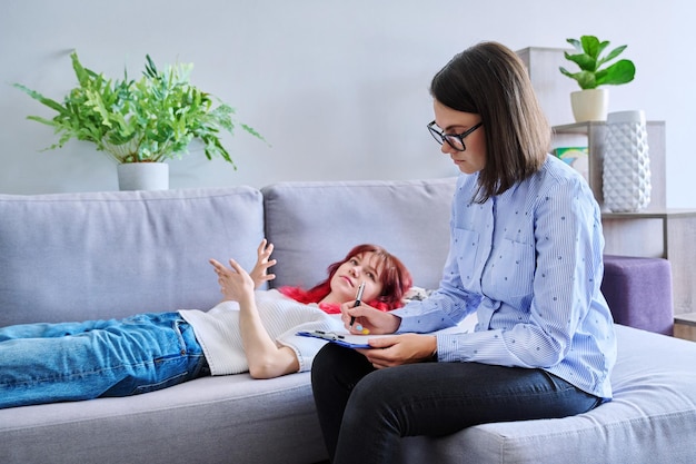 Sesión de terapia de una estudiante adolescente con un psicólogo de asesoramiento Una adolescente acostada en el sofá hablando de problemas de salud mental Terapia psicológica de la adolescencia Psicoterapia de ayuda profesional