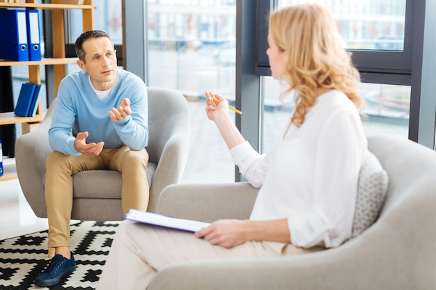 Sessão psicológica. homem bonito, simpático e agradável olhando para sua psicóloga e conversando com ela enquanto discutia seu problema