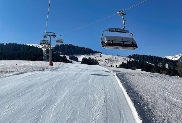 Sessellift mit Schnee und Bäumen unter dem blauen sonnigen Himmel in Österreich