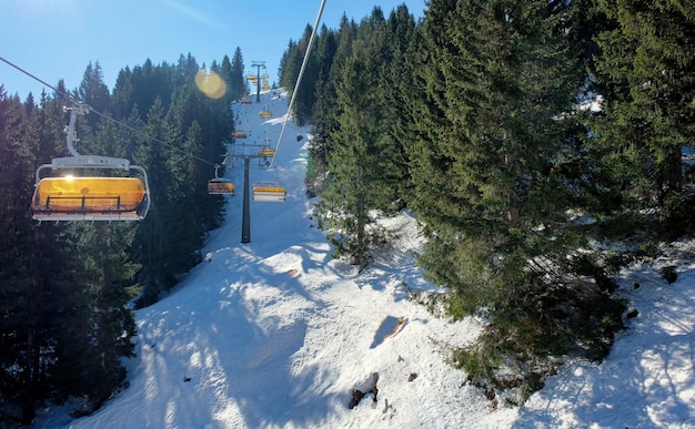 Sessellift mit Schnee und Bäumen unter dem blauen sonnigen Himmel in Österreich