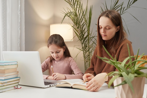 Foto sessões de aprendizagem on-line em conjunto participar de webinars escolares menina com professor usando laptop enquanto está sentada na mesa em casa fazendo tarefas com livro e livro de exercícios