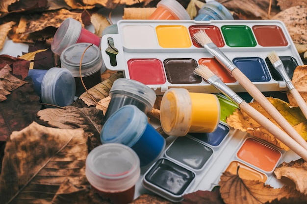 Set aus Aquarellfarben und Pinseln zum Malen von Nahaufnahmen auf dem Hintergrund von Herbstblättern