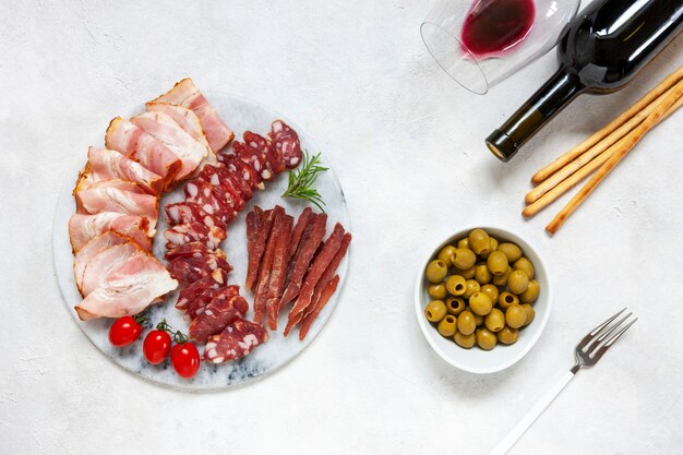 Set aus geräuchertem Speck, Salami und Basturma, serviert mit eingelegten Oliven, Tomaten, Wein und Grissini-Brot