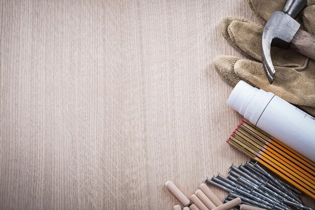 Set aus Holzmeterdübeln Baupläne Klauenhammer braune Schutzhandschuhe und Metallnägel auf Holzbrett Kopierraum Wartungskonzept