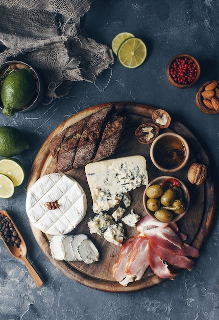 Set aus Käsehamon, Honig, grünen Oliven, Nüssen und Gewürzen auf rustikalem Holzbrett, verschiedene Snacks