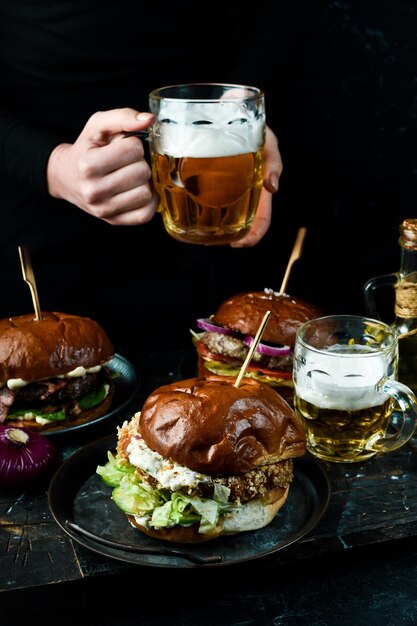 Foto set aus leckeren burgern und bier in einem glas. auf dunklem hintergrund.