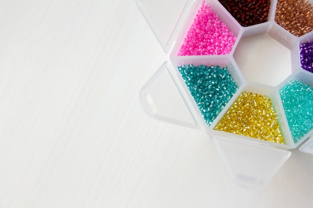 Set aus Perlen und Glasperlen in verschiedenen Farben im Behälter auf Holzuntergrund