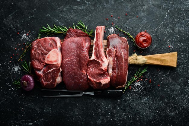 Set aus rohen Rind- und Kalbssteaks Fleisch Draufsicht Flache Draufsicht auf schwarzem Steinschneidetisch