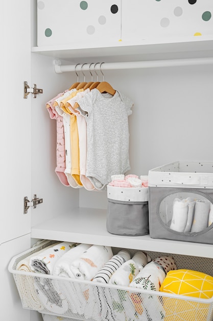 Set Babybodys für ein neugeborenes Mädchen und einen Jungen auf Kleiderbügeln im weißen Kleiderschrank. Mutterschaft, Reinigung der Kindergarderobe. Minimales Modekonzept.