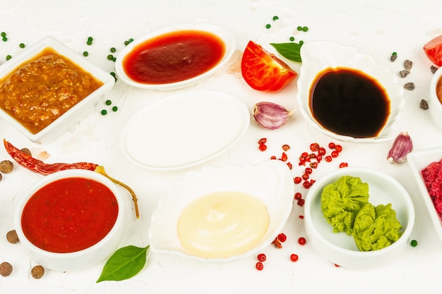 Set mit verschiedenen Saucen - Ketchup, Mayonnaise, Barbecue, Soja, Chutney, Wasabi, Adjika, Meerrettich, Aioli, Marinara. Trendiges hartes Licht, dunkler Schatten. Weißer Kitthintergrund, Draufsicht