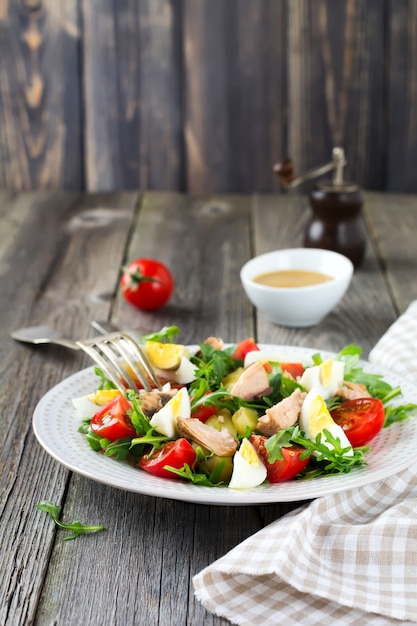 Set Rohstoffe Kartoffeln, Eier, frischer Rucola, Olivenöl, Pfeffer, Thunfischkonserven, Kirschtomaten, Salz, um einen Salat Nicoise auf der alten Holzoberfläche zuzubereiten