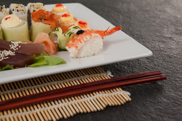 Foto set de sushi surtido servido con palillos en plato blanco sobre estera de sushi