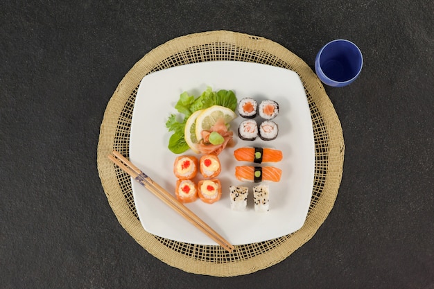 Set de sushi variado servido con palillos y vidrio en estera de sushi