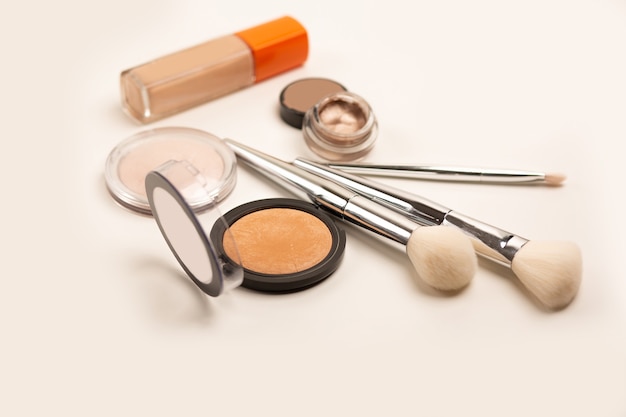 Set de tez: base, polvos compactos, bronceador y brochas sobre fondo gris