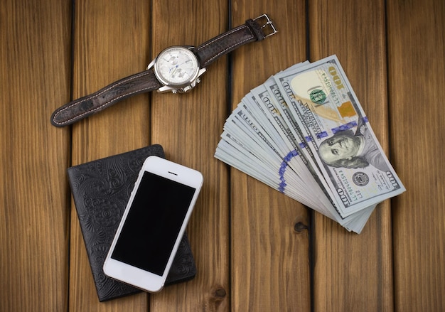 Set von Herrensachen aus einer Uhr und einem Smartphone mit Geld auf einem Holz