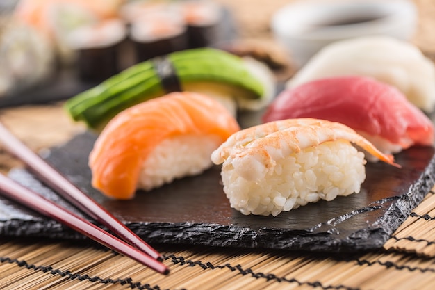 Set von Nigiri-Sushi auf Schieferbrett mit Stäbchen.