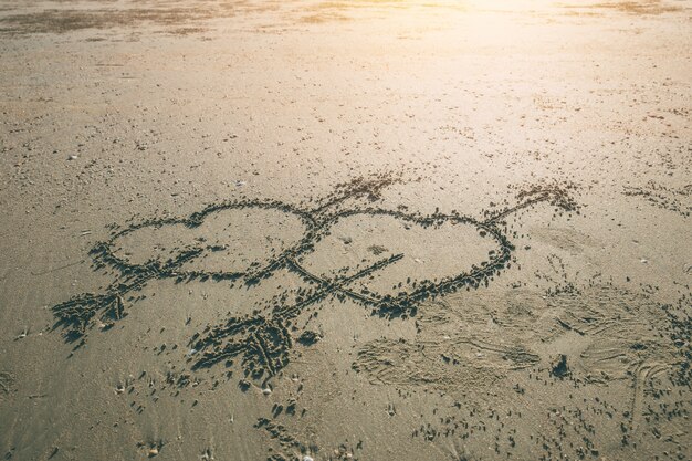 Seta de coração amor gêmeo de símbolo de cupido desenhar na praia do mar com fundo por do sol