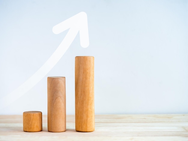 Seta para cima em paus redondos de madeira como etapas de gráfico de negócios isoladas em mesa de madeira em fundo branco com espaço de cópia Conceitos de sucesso do processo de gráfico de crescimento de negócios e melhoria econômica