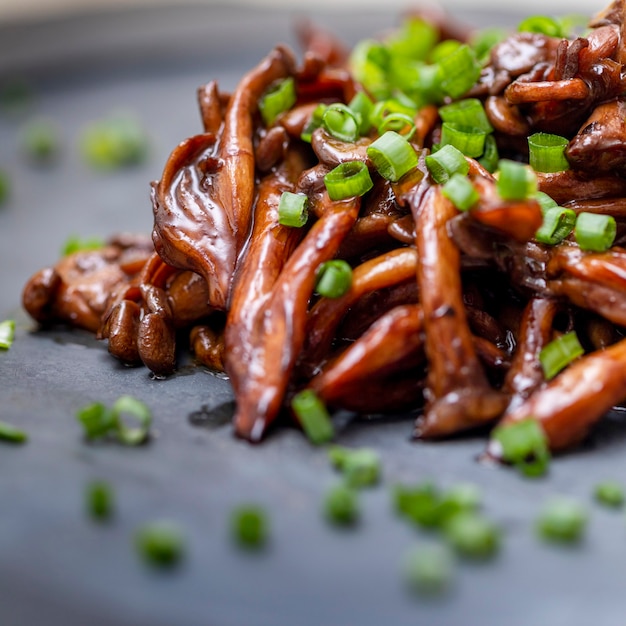 Seta shimeji servida con cebollino en plato de piedra negra. Comida típica oriental. Detalle del plato de comida, primer plano, enfoque selectivo.