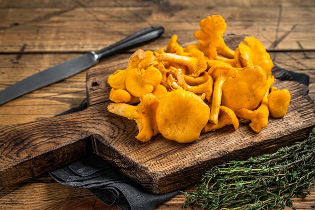 Setas de chanterelles salvajes crudas sin cocer en una tabla de cortar Fondo de madera Vista superior