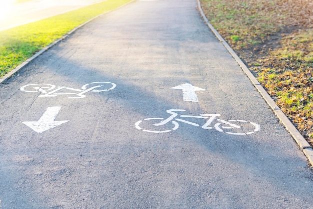 Setas de direção de marcações bidirecionais de uma ciclovia na calçada, sinal de bicicleta pintado de branco na estrada em um parque da cidade. ícone de uma bicicleta no asfalto. ciclismo, atividade esportiva e estilo de vida saudável.